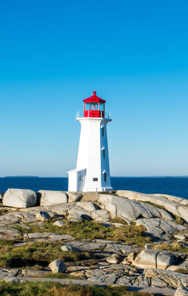 Pictured is the Peggy's cove lighthouse in Nova Scotia. in the center is a white lighthouse with a red roof in front of the sea.