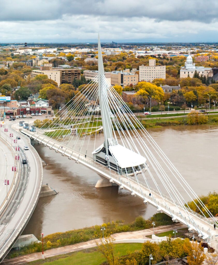 Pictured is an aerial view of a river, bridge, and lush green landscape in Winnipeg, Manitoba